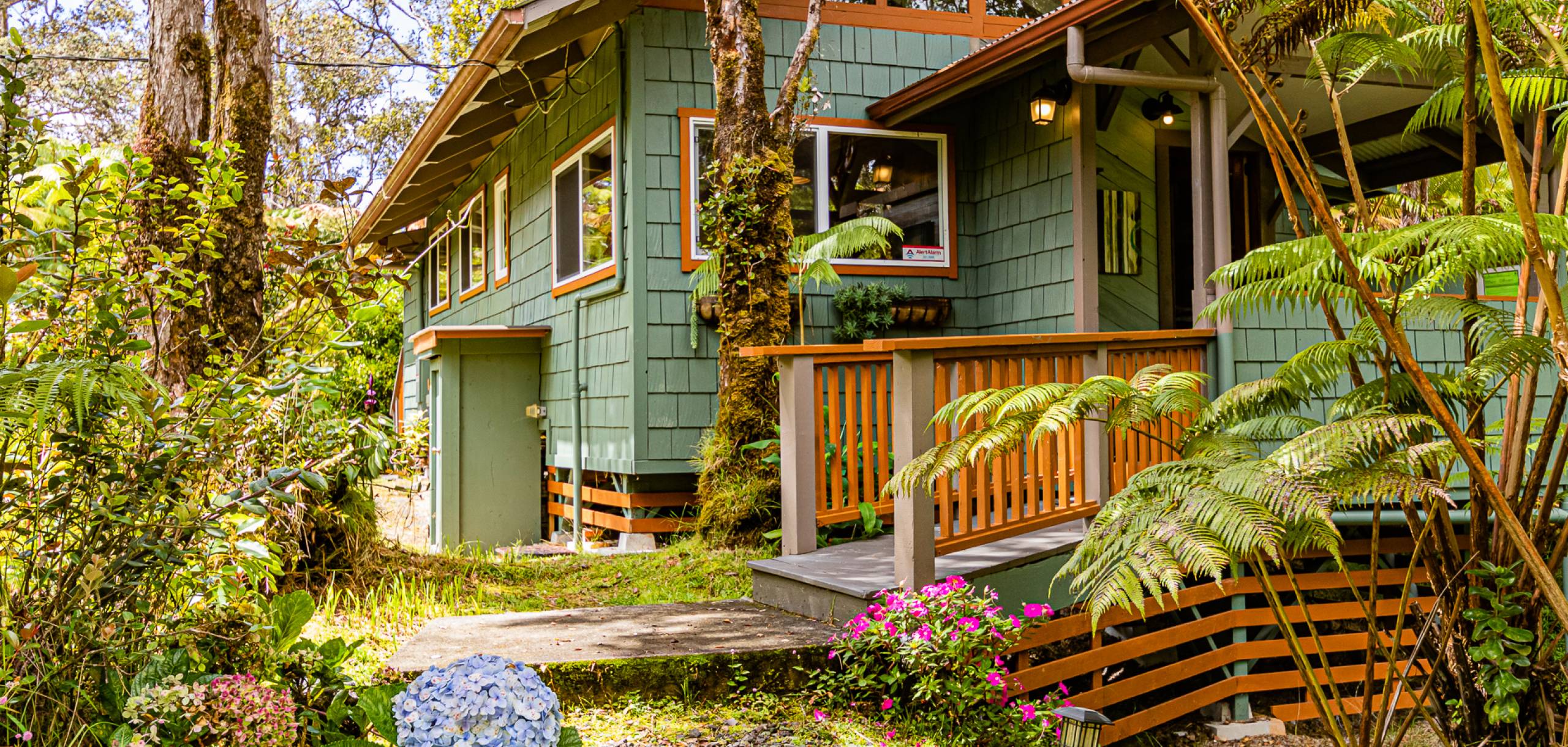 Green cottage in Volcano, Hawaii surrounded by trees and flowers